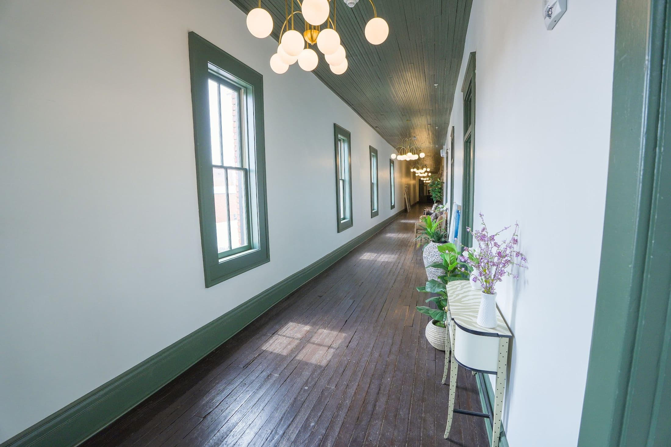 The restored corridor at The Whistlestop, with green wainscoting, a pressed-tin ceiling and brass globe chandeliers